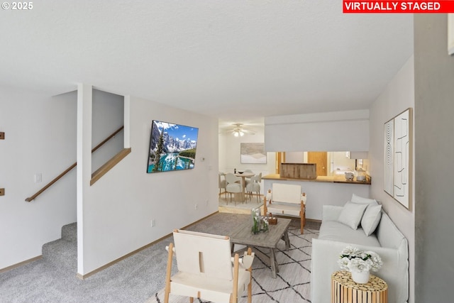 carpeted living room featuring baseboards, stairs, and ceiling fan