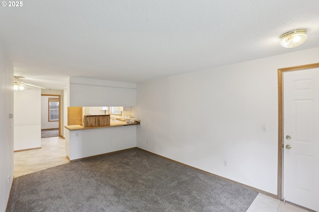 unfurnished living room with a ceiling fan, baseboards, and light colored carpet