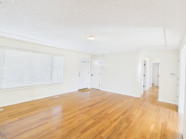 spare room with light wood-style flooring, a textured ceiling, and baseboards