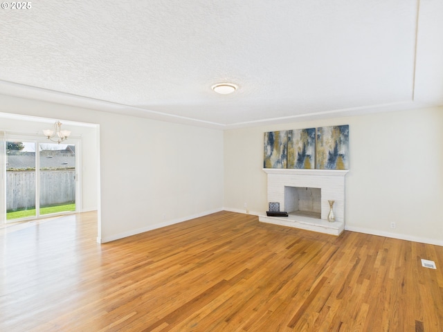 unfurnished living room featuring baseboards, a fireplace, an inviting chandelier, light wood-style floors, and a textured ceiling