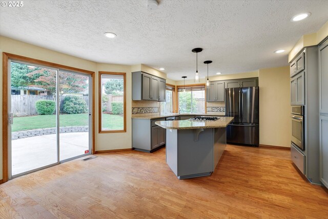 kitchen featuring a kitchen island, gray cabinetry, appliances with stainless steel finishes, and light wood-style floors