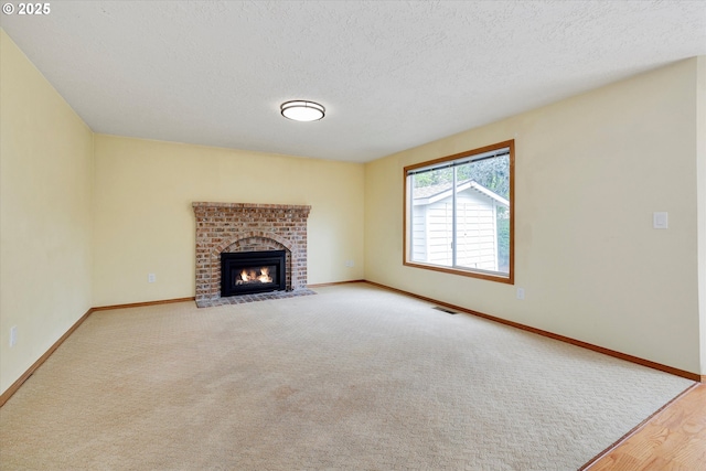 unfurnished living room with baseboards, a brick fireplace, a textured ceiling, and visible vents