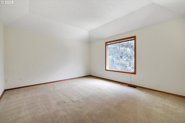 empty room featuring visible vents, baseboards, vaulted ceiling, and carpet