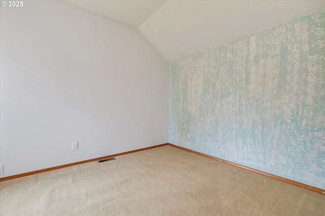empty room featuring visible vents, carpet flooring, baseboards, and vaulted ceiling