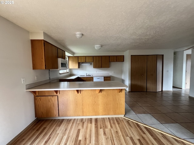 kitchen featuring brown cabinets, light countertops, a sink, white appliances, and a peninsula