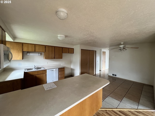 kitchen featuring light tile patterned floors, brown cabinetry, white dishwasher, a sink, and a peninsula