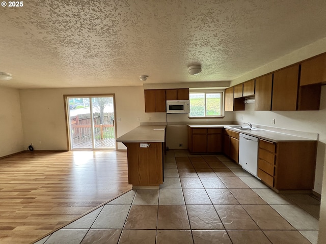 kitchen featuring white appliances, light wood-style flooring, light countertops, a textured ceiling, and a sink