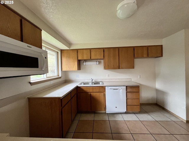 kitchen with light tile patterned floors, white appliances, a sink, light countertops, and brown cabinetry