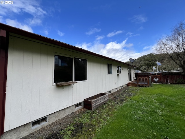 view of property exterior with a lawn, a wooden deck, and fence