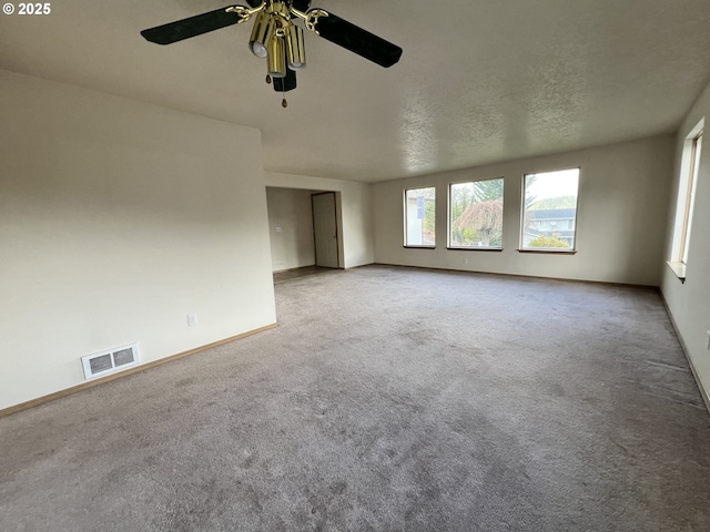 carpeted empty room with baseboards, visible vents, ceiling fan, and a textured ceiling