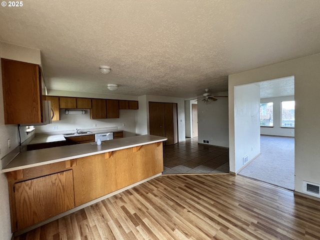 kitchen with dishwasher, a peninsula, light countertops, and light wood-style flooring