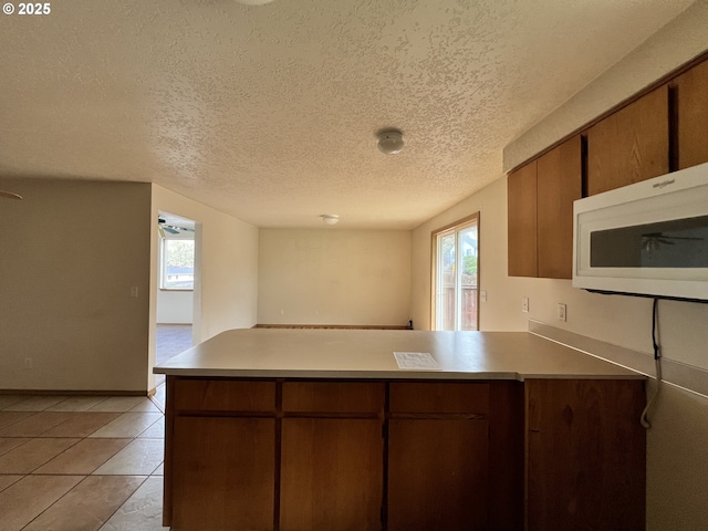 kitchen featuring a peninsula, white microwave, light tile patterned flooring, and light countertops