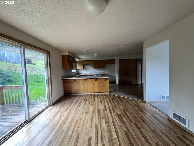 kitchen featuring light wood-style flooring, light countertops, visible vents, and a peninsula