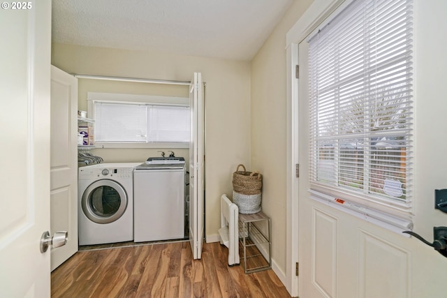 clothes washing area with laundry area, wood finished floors, washing machine and clothes dryer, and baseboards