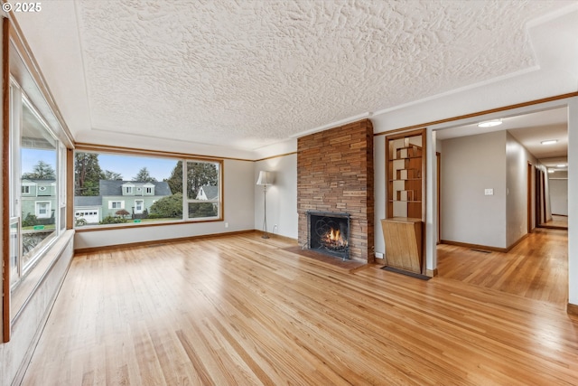 unfurnished living room featuring baseboards, ornamental molding, wood finished floors, a textured ceiling, and a stone fireplace