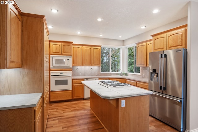 kitchen with stainless steel appliances, tile countertops, light wood-type flooring, tasteful backsplash, and a kitchen island