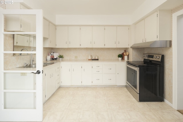 kitchen with light floors, under cabinet range hood, light countertops, stainless steel range with electric stovetop, and a sink