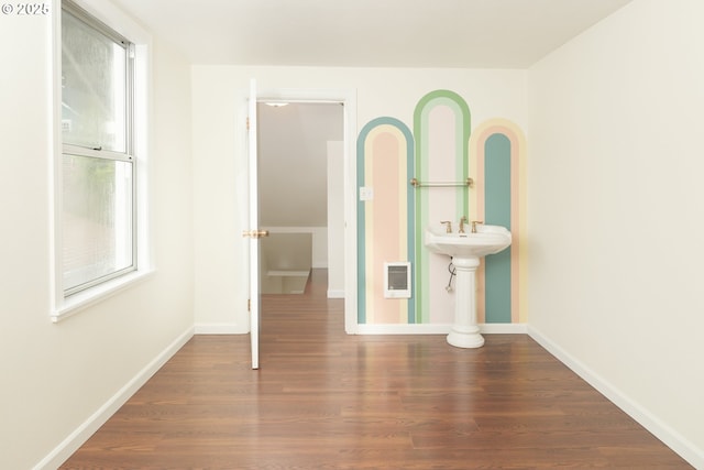 spare room featuring heating unit, baseboards, and wood finished floors