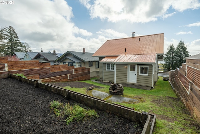 rear view of house with a fire pit, metal roof, a lawn, and fence