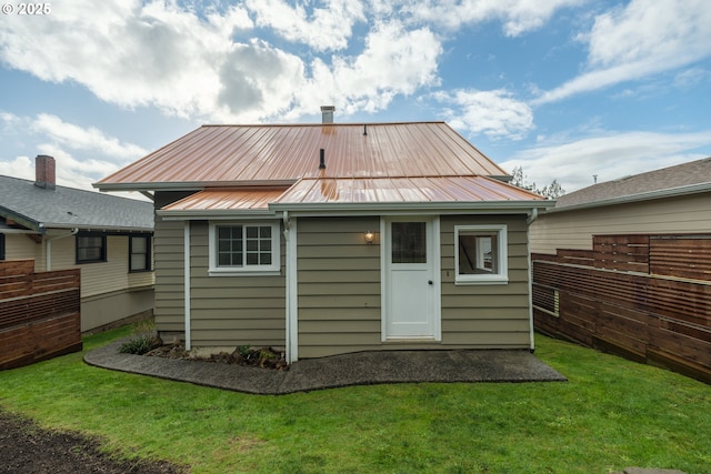 back of property featuring metal roof, fence, and a lawn