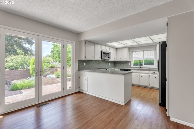 8085 SW Fairway Dr, Wilsonville, OR 97070 - kitchen featuring stainless steel microwave, freestanding refrigerator, a peninsula, white cabinets, and light wood-style flooring