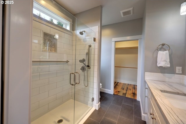 bathroom with a walk in closet, tile patterned flooring, toilet, visible vents, and a stall shower