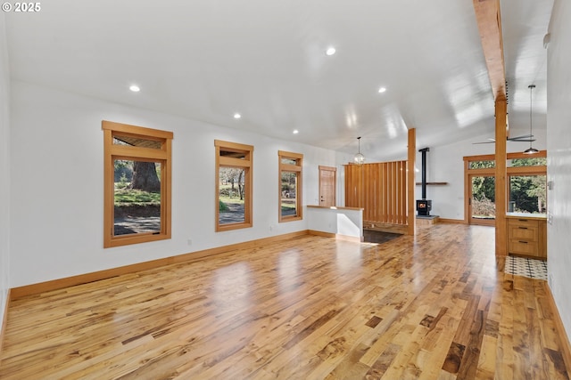 unfurnished living room with lofted ceiling with beams, a wood stove, plenty of natural light, and wood finished floors