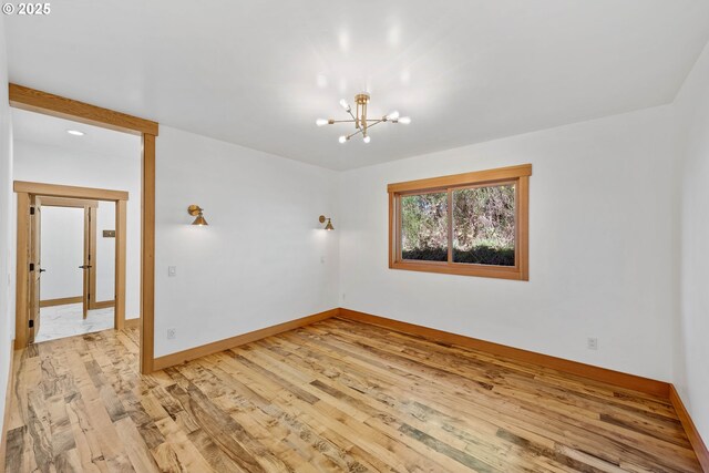 empty room featuring a chandelier, baseboards, and light wood finished floors