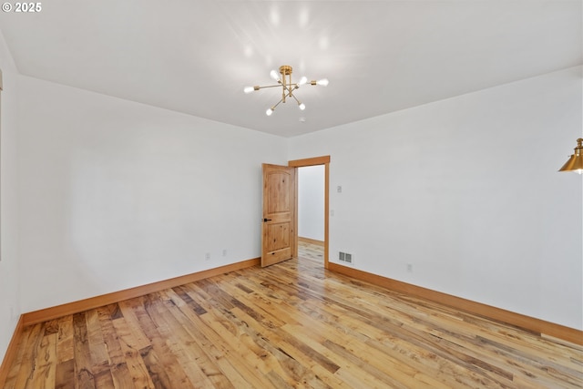 unfurnished room featuring an inviting chandelier, light wood-style flooring, visible vents, and baseboards