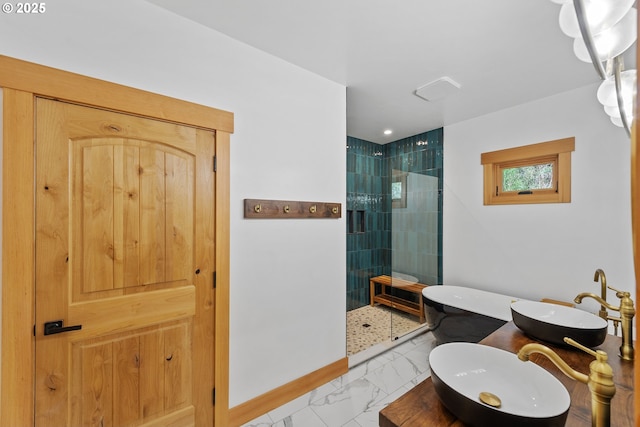 bathroom featuring marble finish floor, dual sinks, baseboards, and a walk in shower