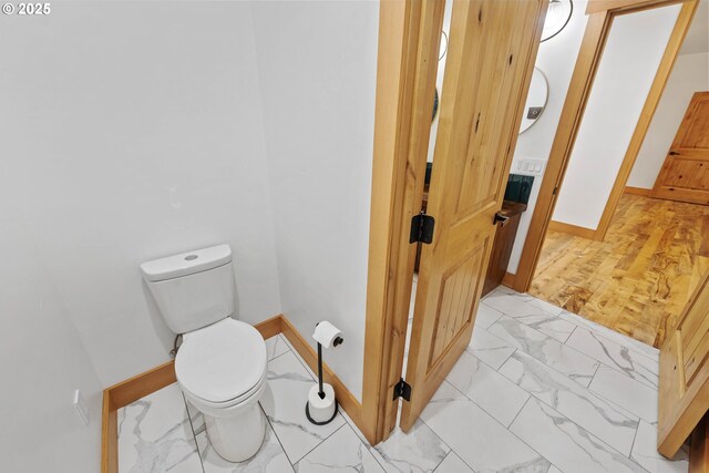 bathroom with marble finish floor, toilet, and baseboards