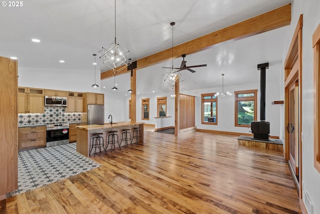 kitchen with light countertops, appliances with stainless steel finishes, beam ceiling, tasteful backsplash, and a wood stove