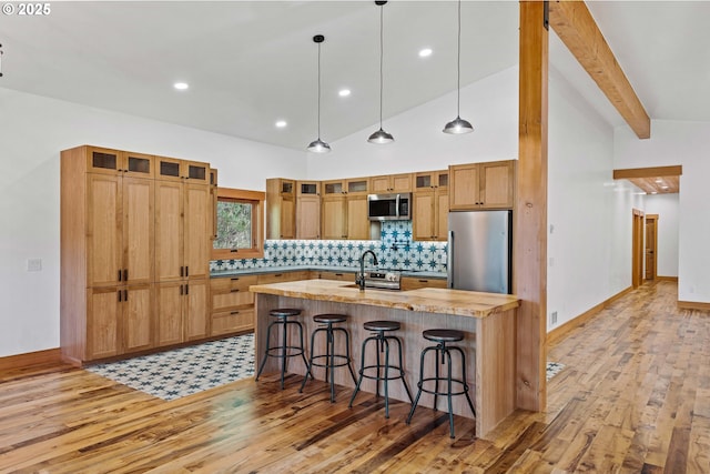 kitchen with light wood finished floors, backsplash, a kitchen breakfast bar, stainless steel appliances, and beam ceiling