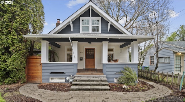 view of front of home with a porch, a chimney, and fence