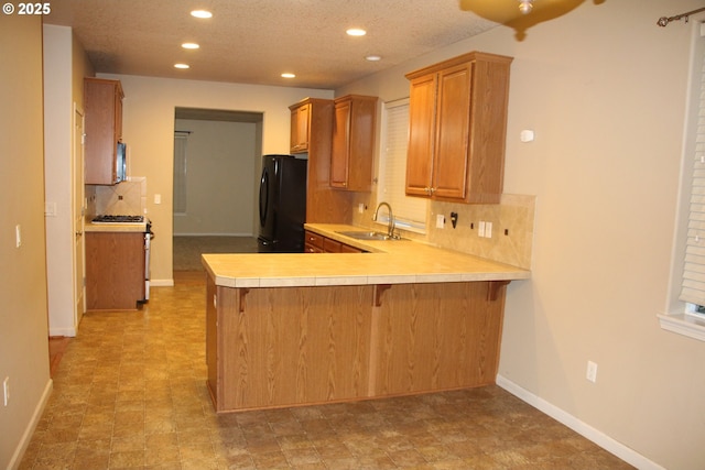 kitchen featuring sink, a breakfast bar area, black refrigerator, tasteful backsplash, and kitchen peninsula