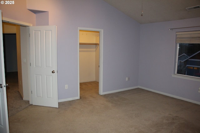 unfurnished bedroom featuring vaulted ceiling, a walk in closet, light colored carpet, and a closet