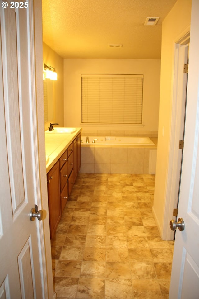 bathroom featuring a relaxing tiled tub, vanity, and a textured ceiling