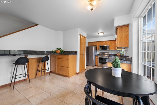 kitchen featuring light tile patterned floors, stainless steel appliances, a sink, a kitchen breakfast bar, and brown cabinetry