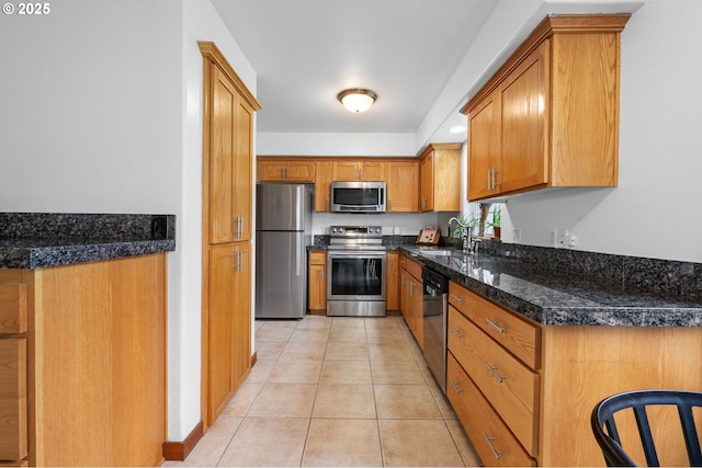 kitchen with light tile patterned floors, stainless steel appliances, a sink, brown cabinetry, and dark countertops