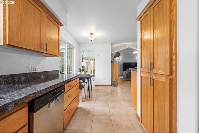 kitchen with light tile patterned floors, baseboards, stainless steel dishwasher, brown cabinets, and dark stone counters