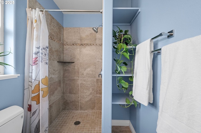 bathroom featuring tiled shower, toilet, and baseboards