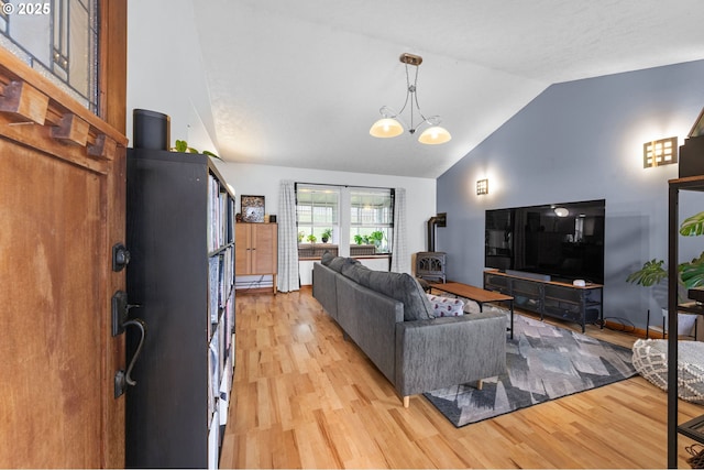 living area with a wood stove, an inviting chandelier, light wood-style flooring, and lofted ceiling