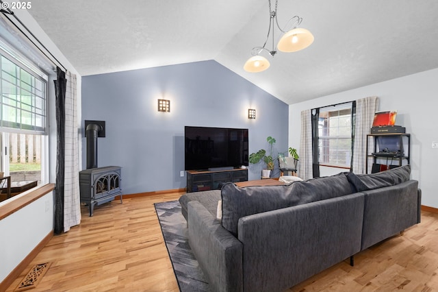 living area featuring light wood finished floors, lofted ceiling, visible vents, a wood stove, and baseboards