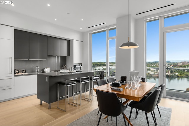 dining room featuring a wealth of natural light, a water view, light hardwood / wood-style flooring, and a wall of windows