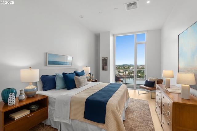 bedroom featuring light wood-type flooring, a water view, and expansive windows