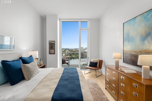 bedroom with expansive windows, a water view, and light hardwood / wood-style flooring