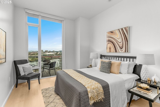 bedroom with multiple windows, light wood-type flooring, access to exterior, and expansive windows