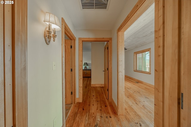 hallway with baseboards, light wood finished floors, and visible vents