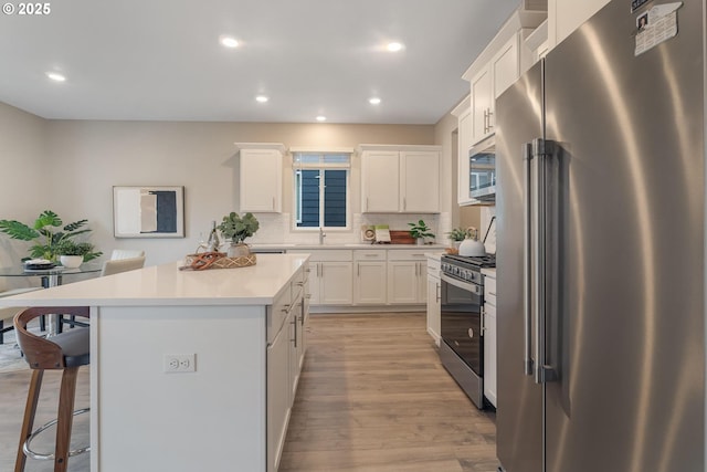 kitchen with white cabinetry, a center island, decorative backsplash, appliances with stainless steel finishes, and light wood-type flooring