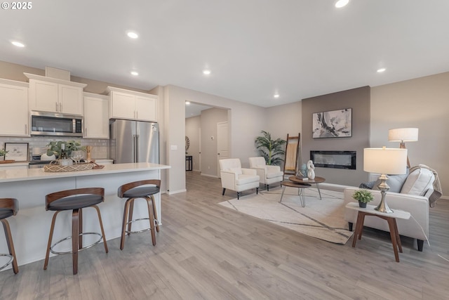 kitchen featuring a kitchen breakfast bar, light wood-type flooring, appliances with stainless steel finishes, tasteful backsplash, and white cabinetry